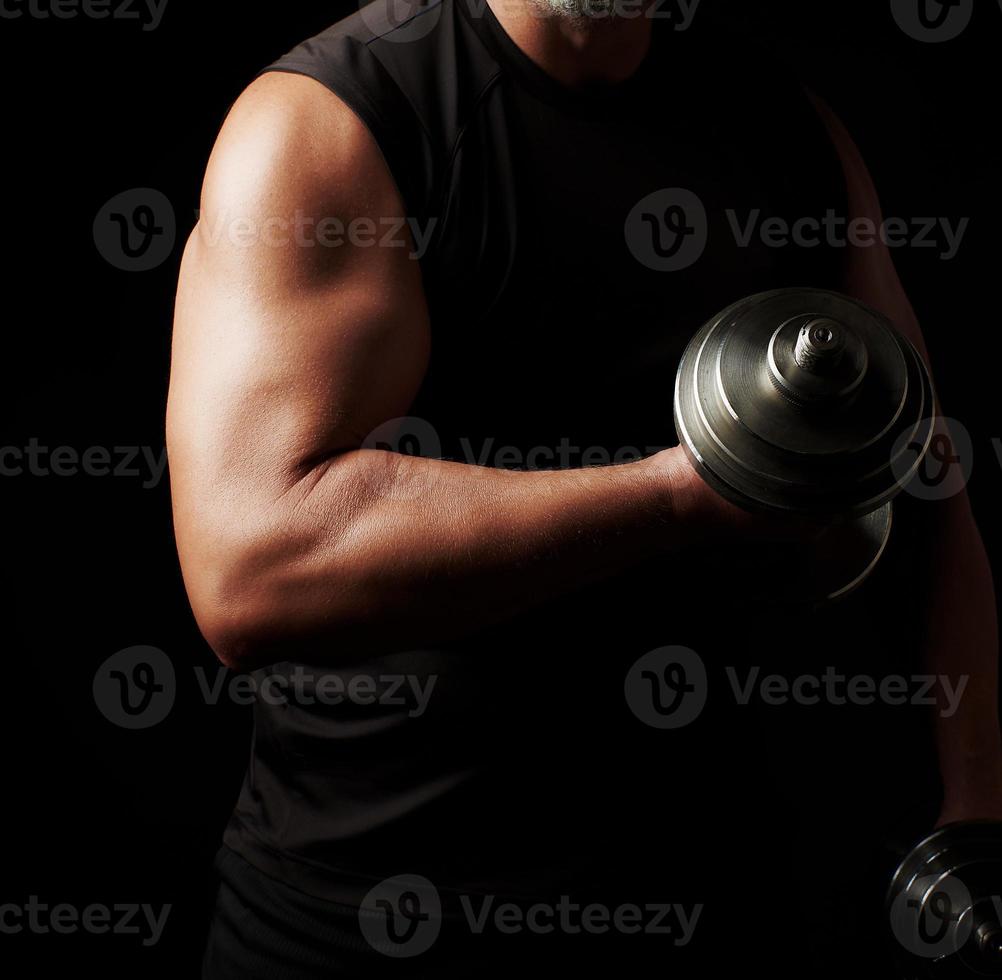 man in black clothes holds steel dumbbells in his hands photo