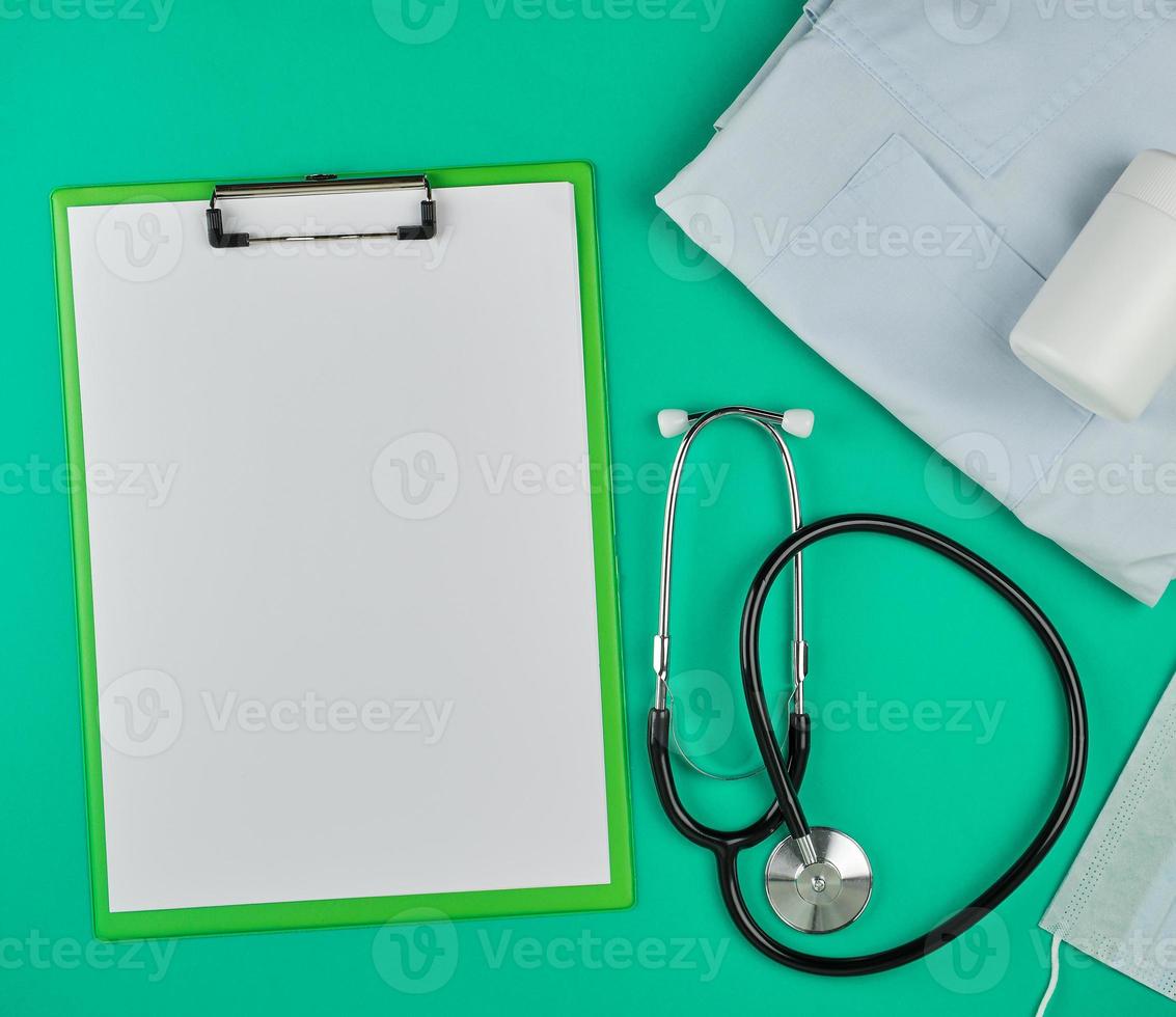 paper holder with empty white sheets, medical stethoscope, pills on a green background photo