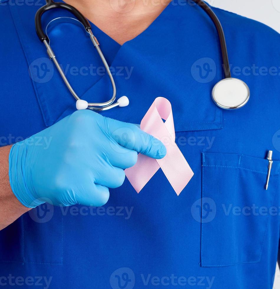 doctor in blue uniform and sterile latex gloves holds a pink ribbon photo