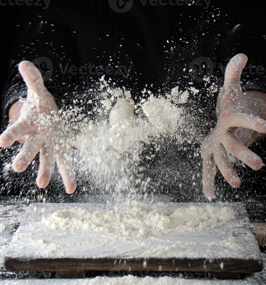 chef in black uniform sprinkles white wheat flour over the table photo
