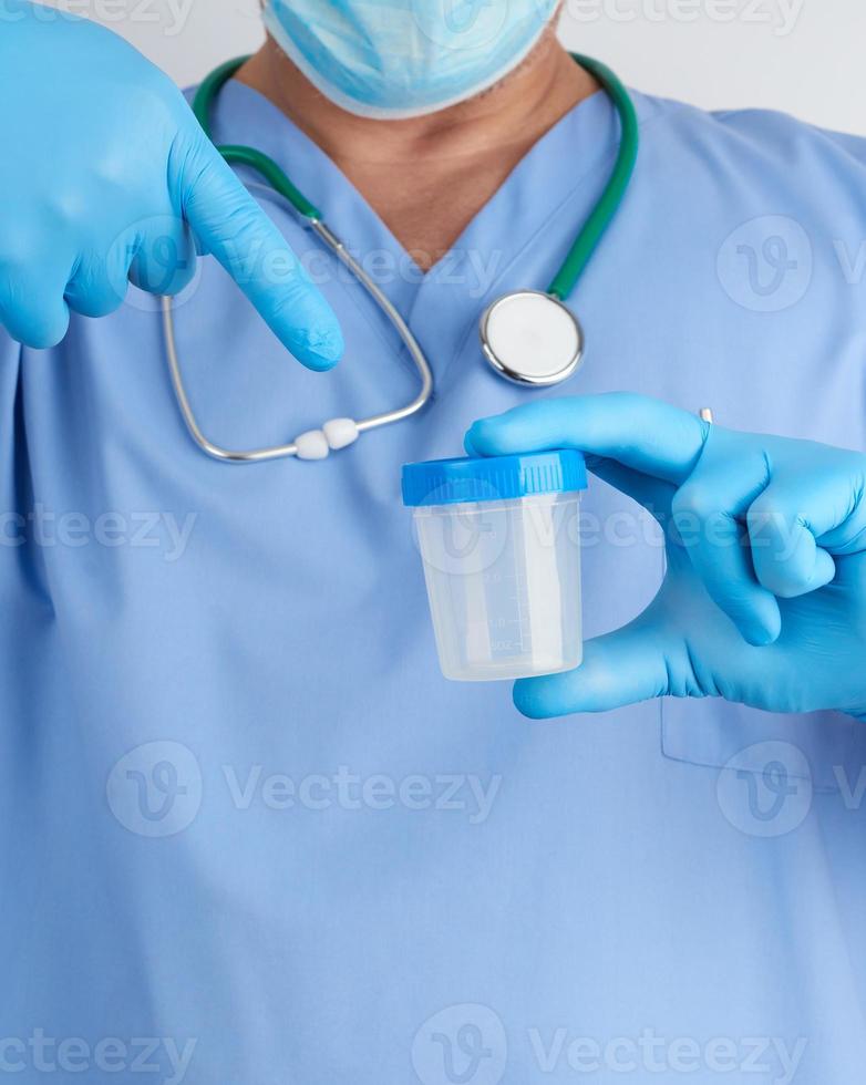 doctor in blue uniform and latex gloves is holding an empty plastic container for taking urine samples photo