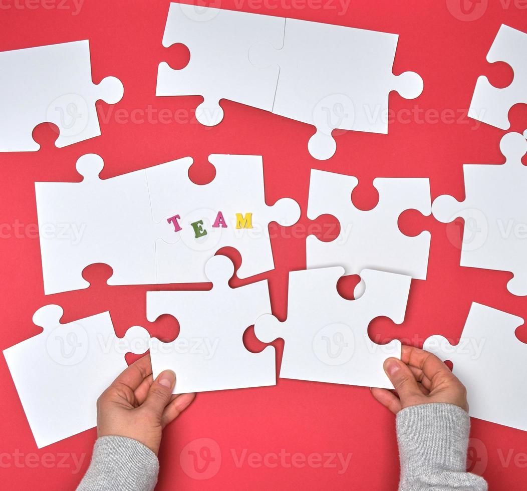 female hand puts white big puzzles on a red background, inscription team photo