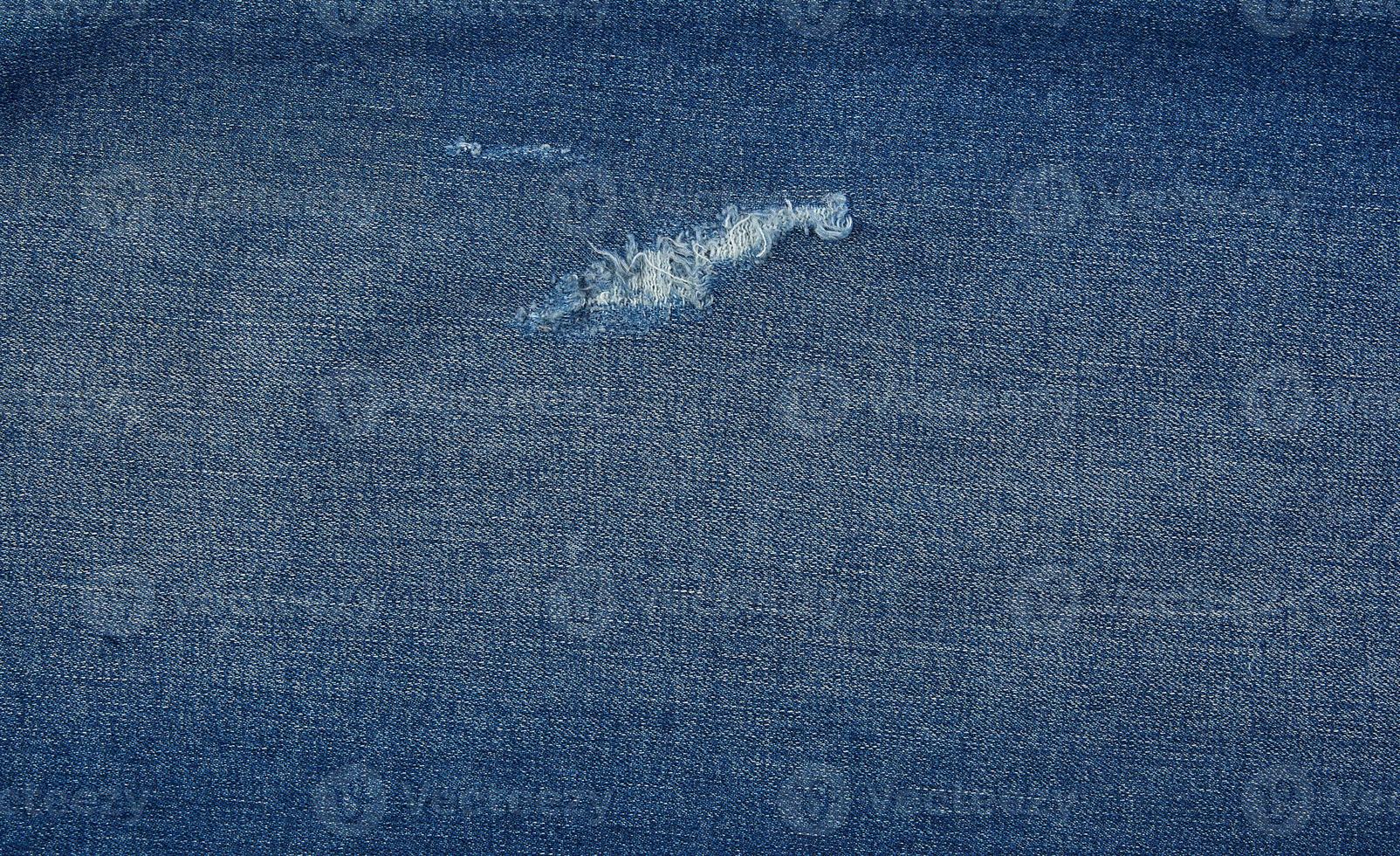 fragment of blue jeans fabric with a hole, full frame photo