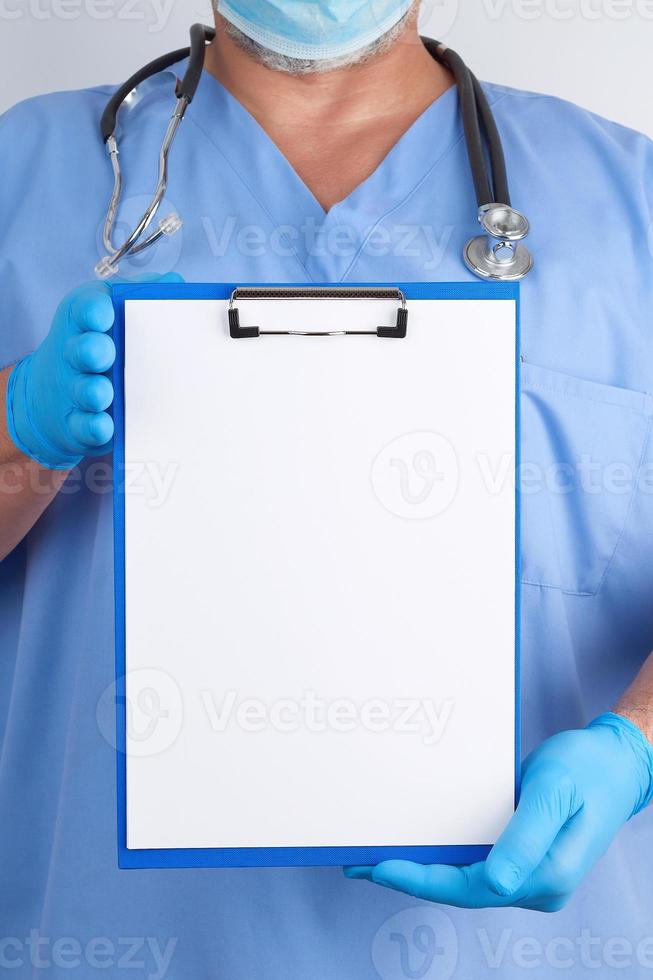 doctor in blue uniform and latex gloves holds a green holder for sheets of paper photo