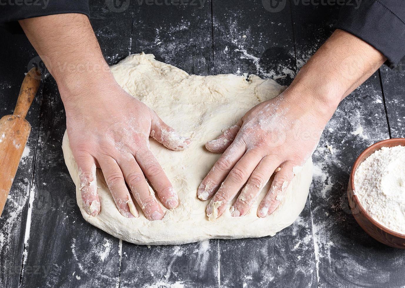 men's hands knead a round piece of dough for making pizza photo