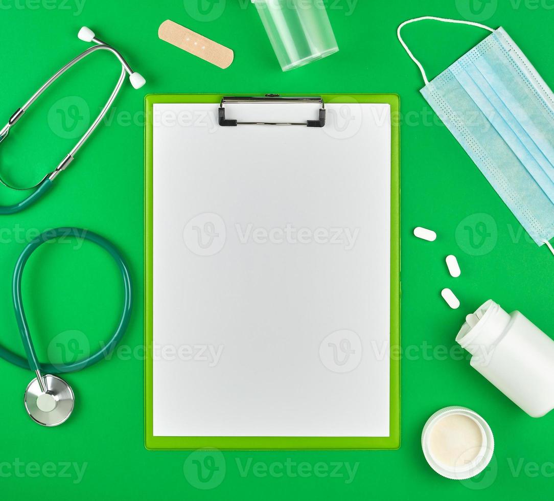 paper holder with empty white sheets, medical stethoscope, pills and textile bandage photo