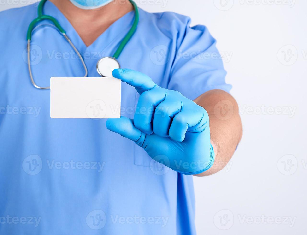 doctor in sterile latex gloves and blue uniform holds a blank white business card photo