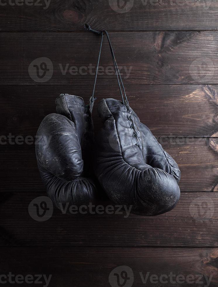 pair of very old shabby black leather boxing gloves hanging on a nail photo