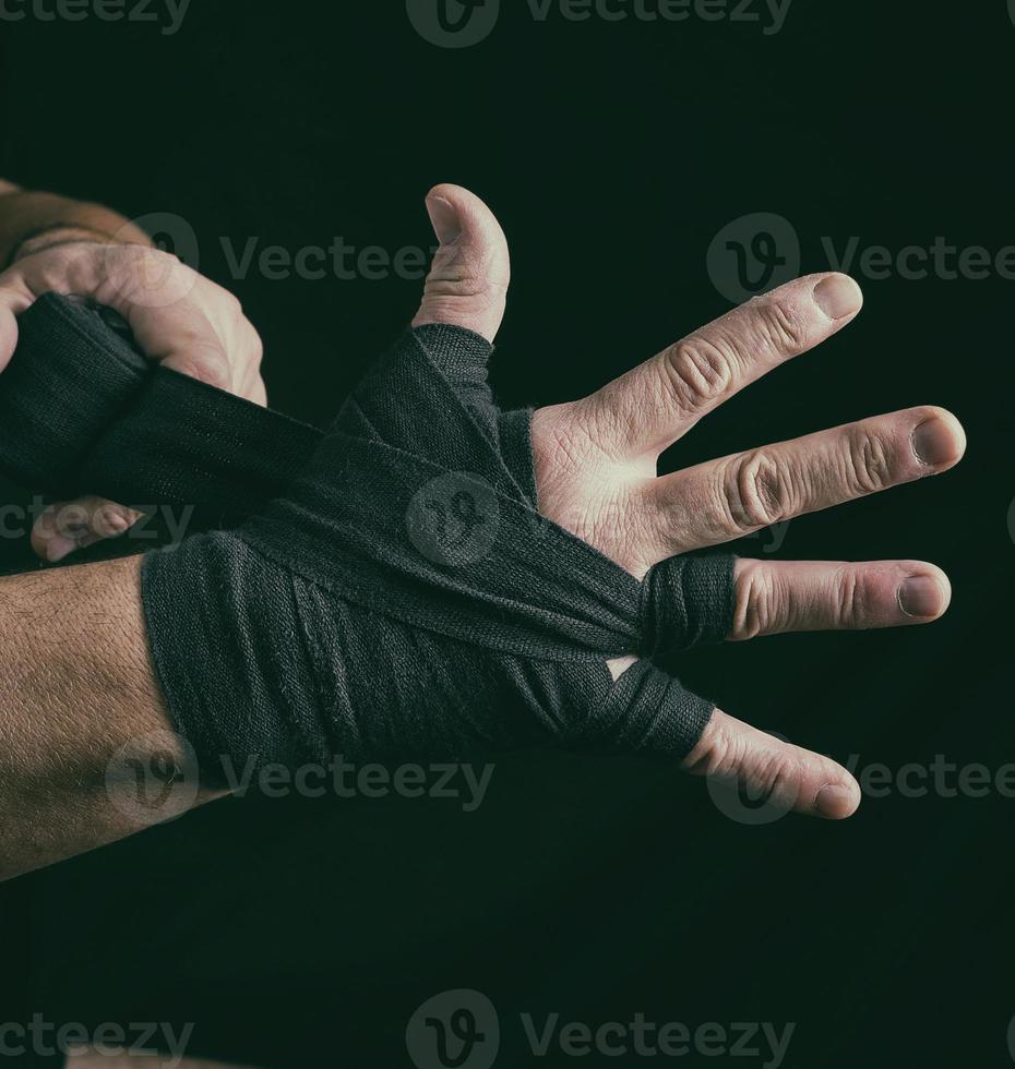 man wraps his hands in black textile bandage for sports photo