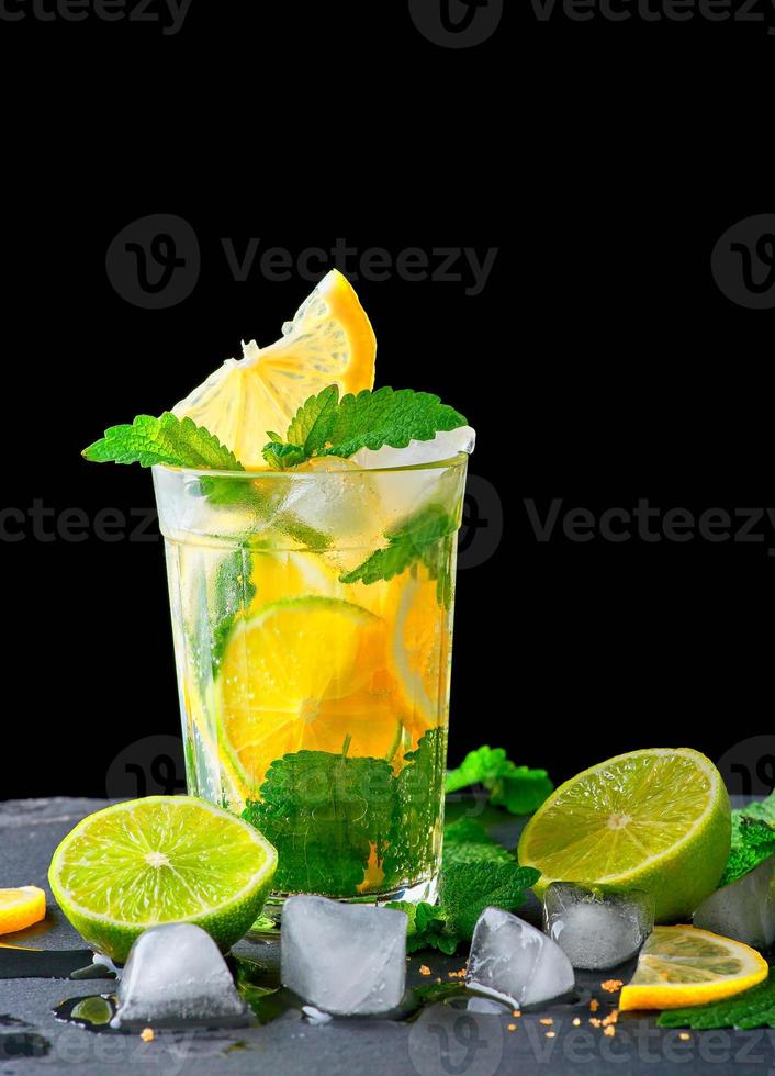 refreshing drink lemonade with lemons, mint leaves, ice cubes and lime in a glass on a black background, copy space photo