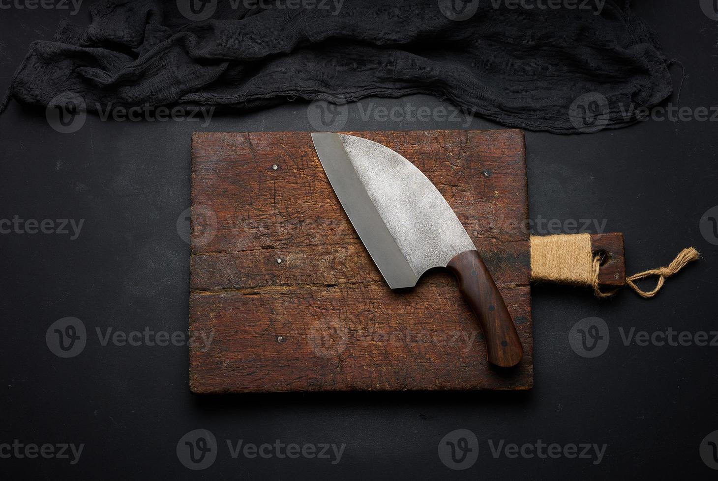 Rectangular empty wooden cutting board and kitchen knife on black table with gauze napkin, top view photo