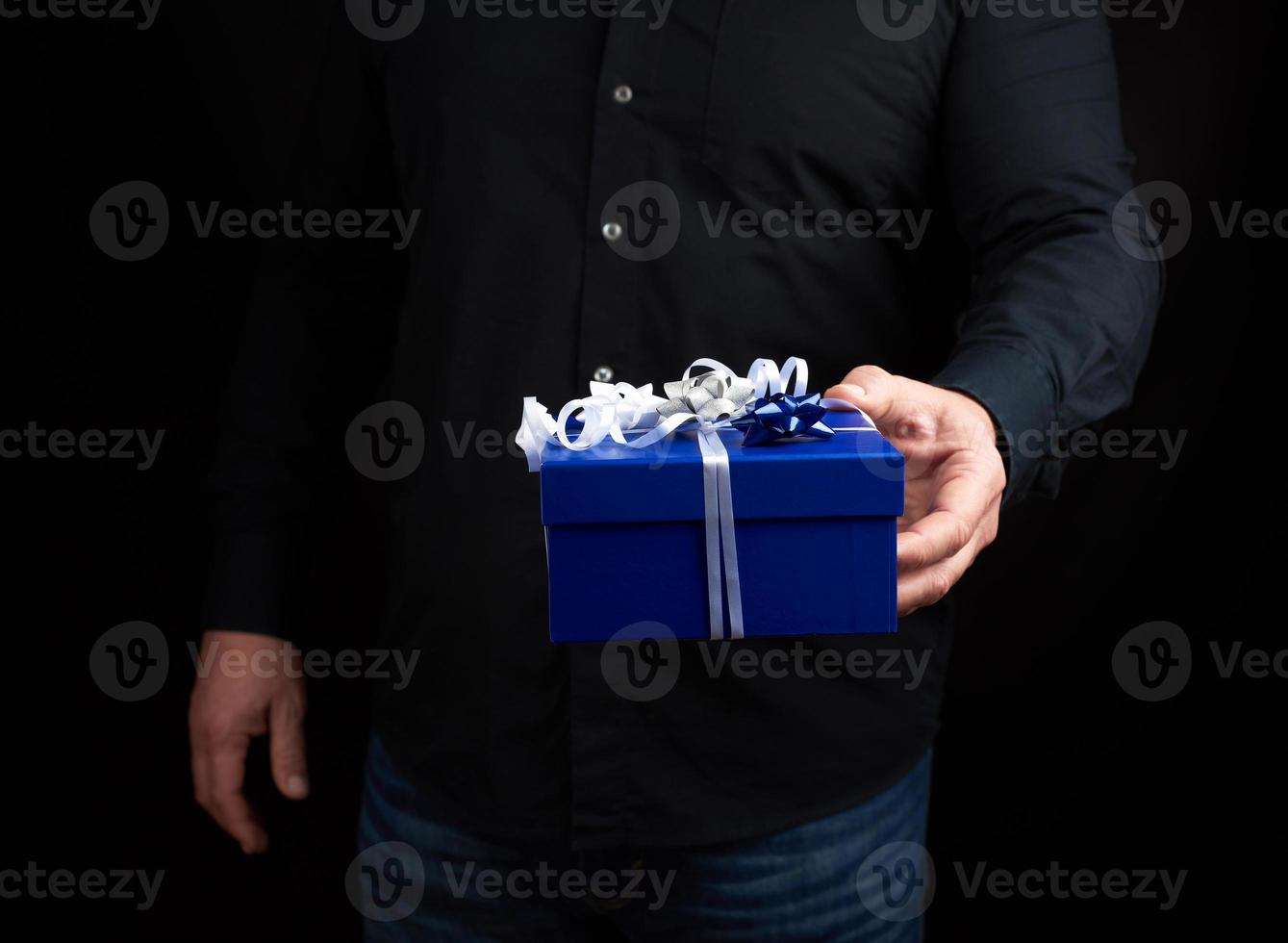 adult man in a black shirt holds a blue square box with a white bow photo