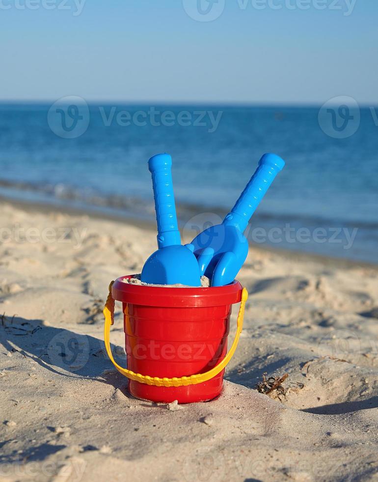 Baby red plastic bucket with sand and shovel on the seashore photo