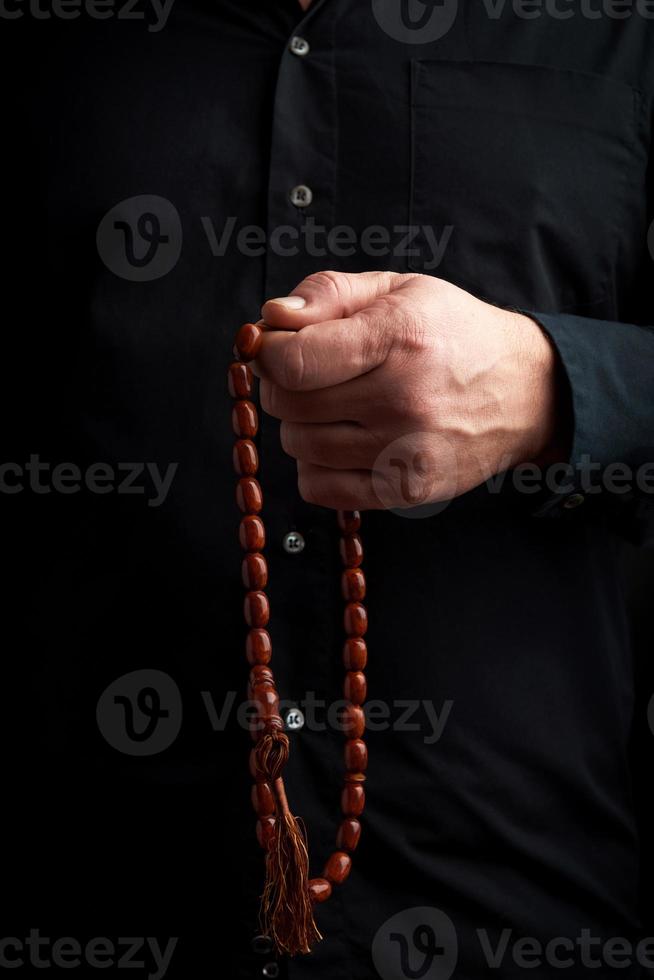 man in a black shirt holds a brown stone rosary in his left hand, low key photo