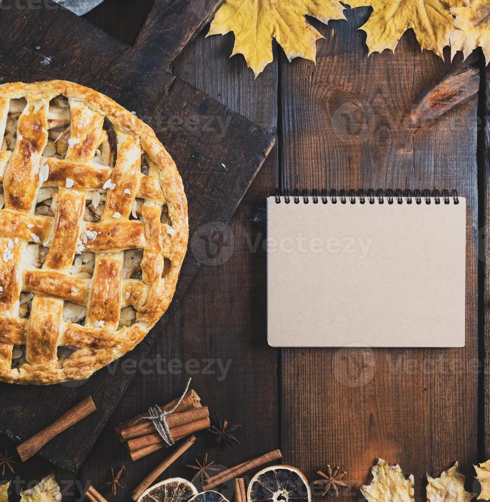 pastel de manzana al horno en un tablero y un cuaderno con una página en blanco para escribir una receta foto
