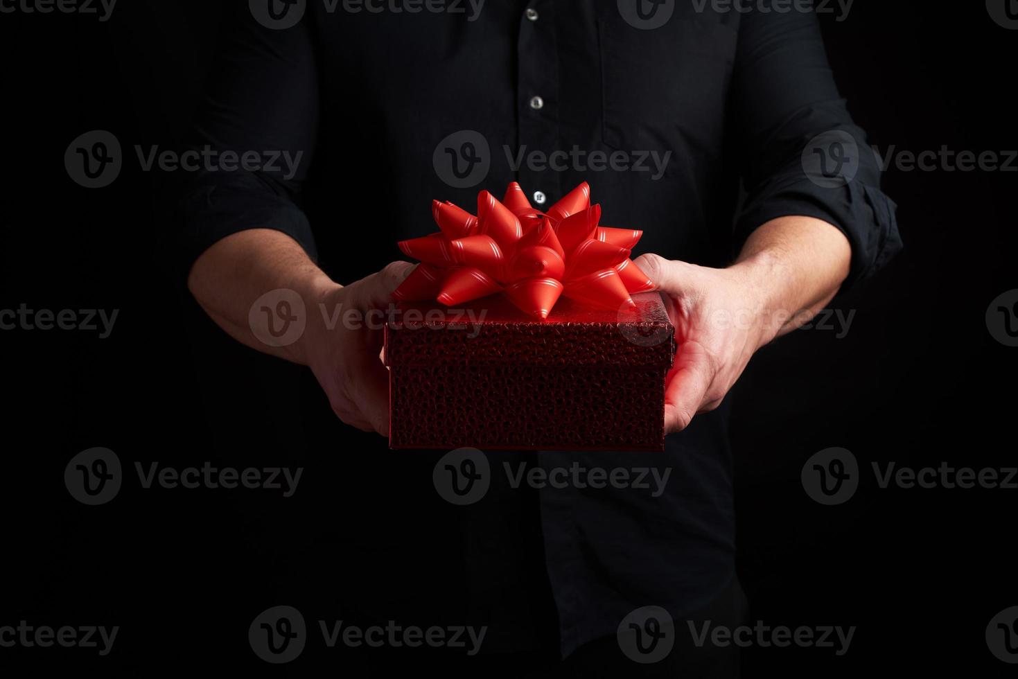 adult man in a black shirt holds a red square box with a knotted bow on a dark background photo