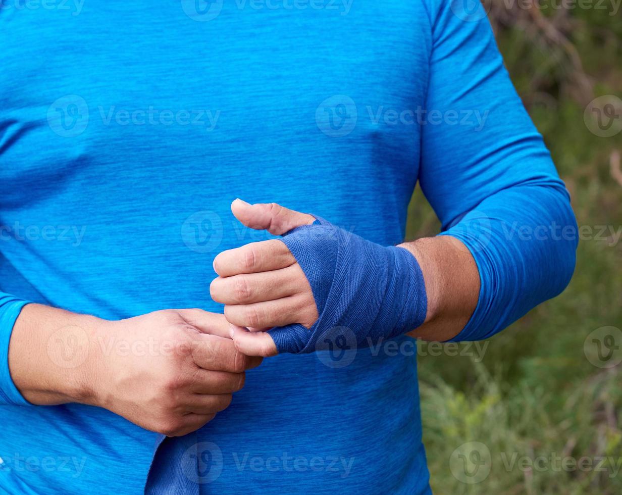 athlete stand and wrap his hands in blue textile elastic bandage photo