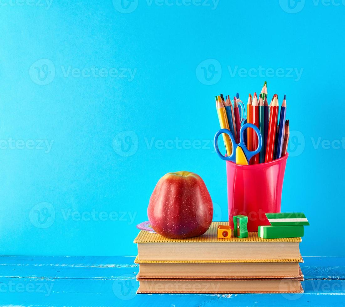red plastic cup with multi-colored wooden pencils stands on a stack of books photo