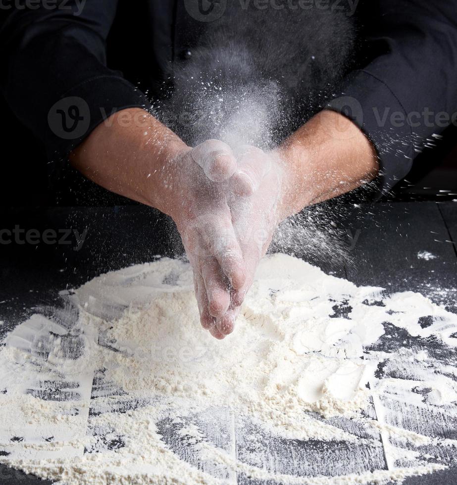 chef in black uniform pours white wheat flour out of his hands on a wooden table photo