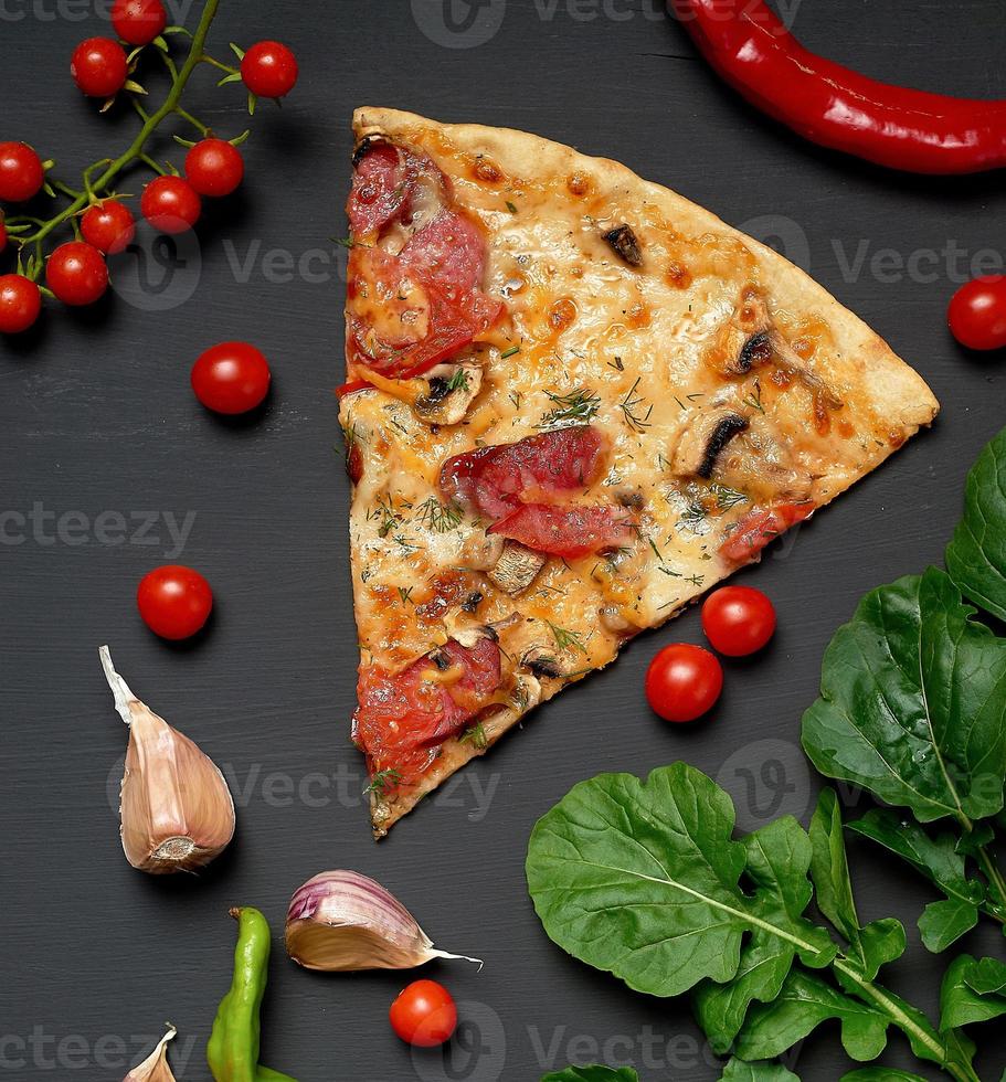triangular slice of baked pizza with mushrooms, smoked sausages, tomatoes and cheese photo