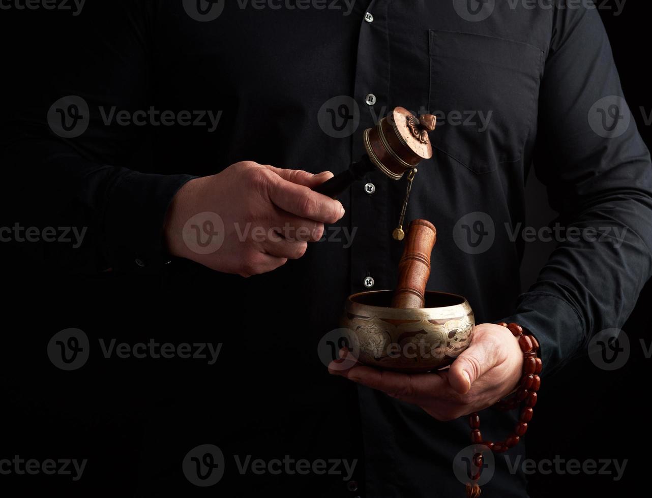 man in a black shirt holds a Tibetan brass singing bowl and a wooden stick photo