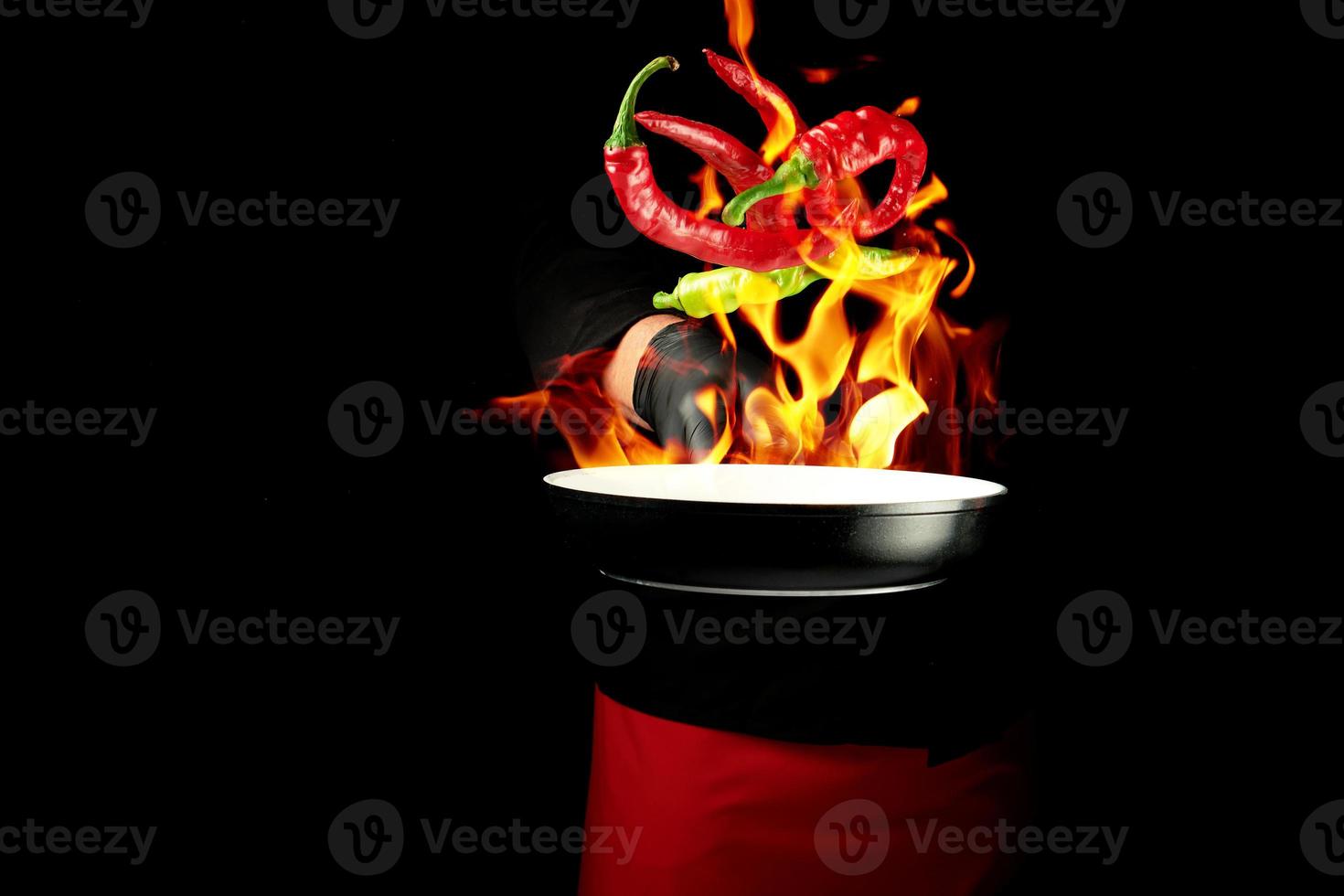 chef in a black uniform holds a round pan and throws up red and green whole chili peppers photo