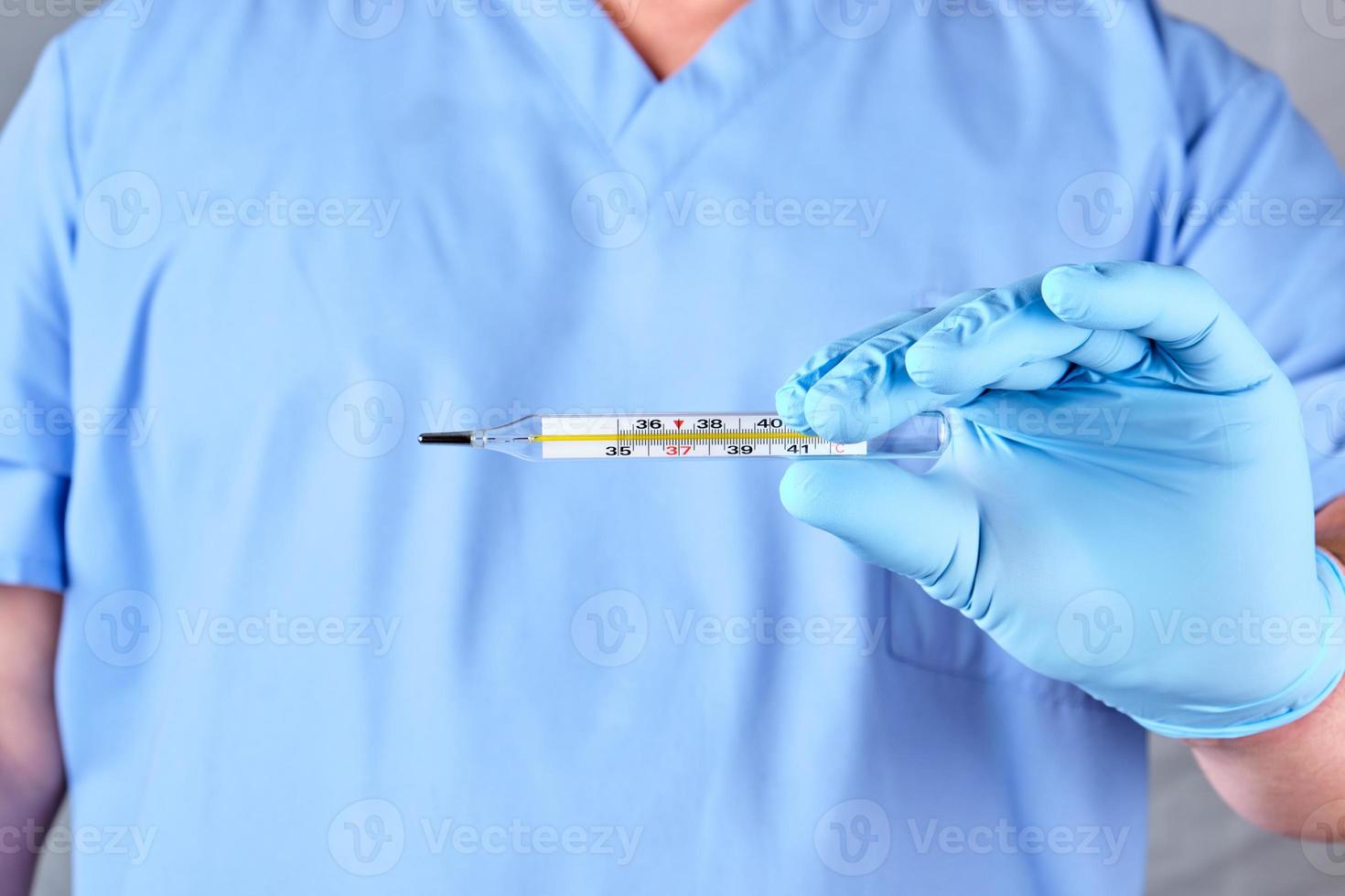 doctor with blue latex gloves and uniform holding a glass mercury thermometer photo