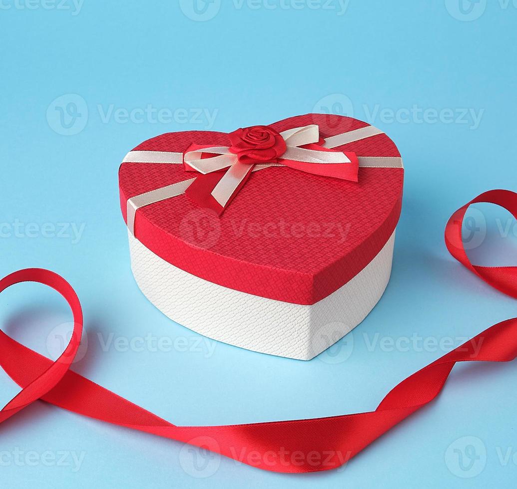 closed red heart-shaped gift box with a bow on a blue background photo