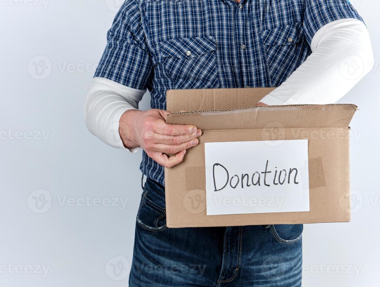 man in a blue checkered shirt and jeans holds a big brown paper box with the inscription donation photo