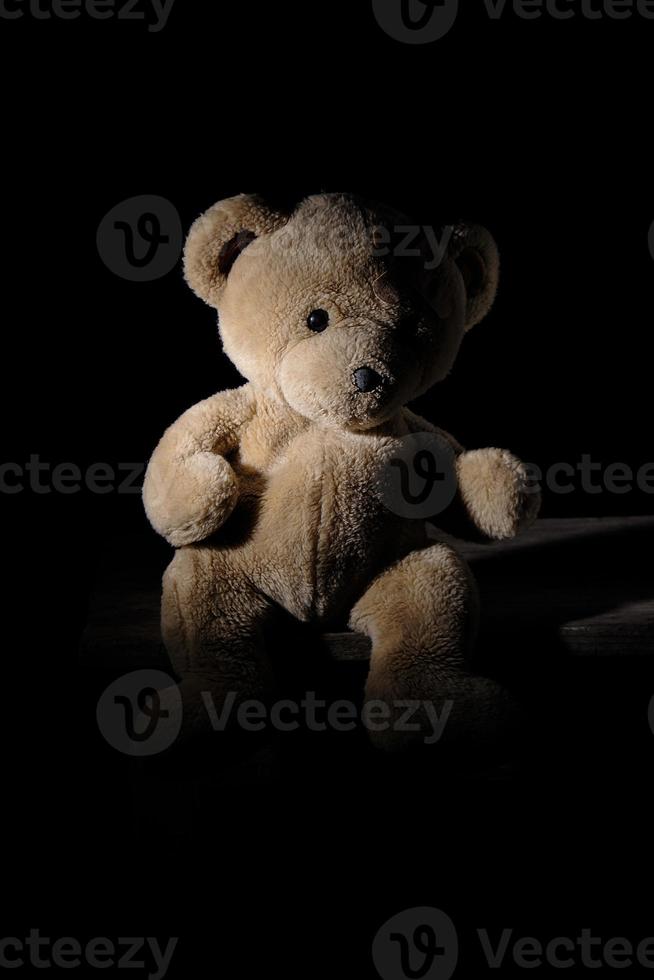 old brown teddy bear is sitting on a wooden surface photo