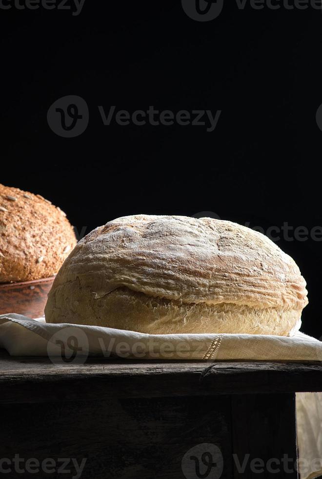 baked round white wheat bread on a textile towel, wooden old table photo
