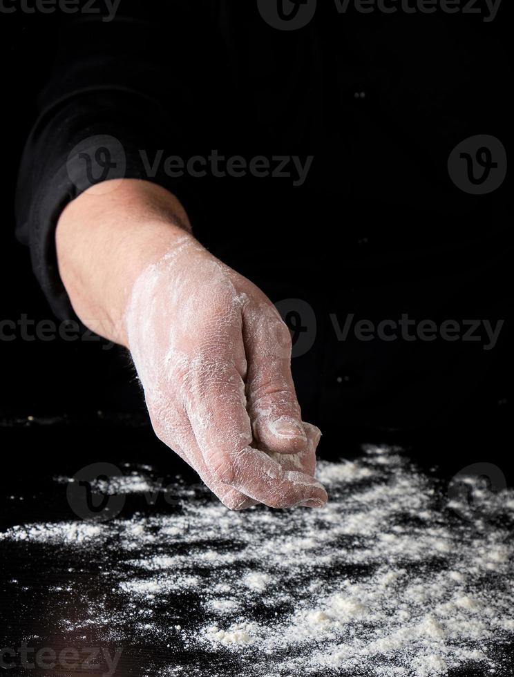 chef in black uniform sifts through his fingers white wheat flour over the table photo