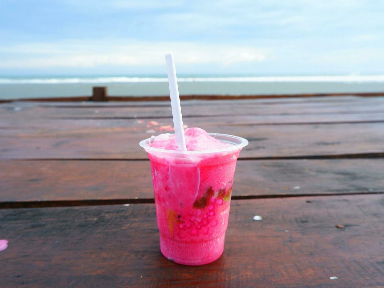 es podeng o bebida rosa sobre una mesa de madera con fondo de playa, indonesia foto