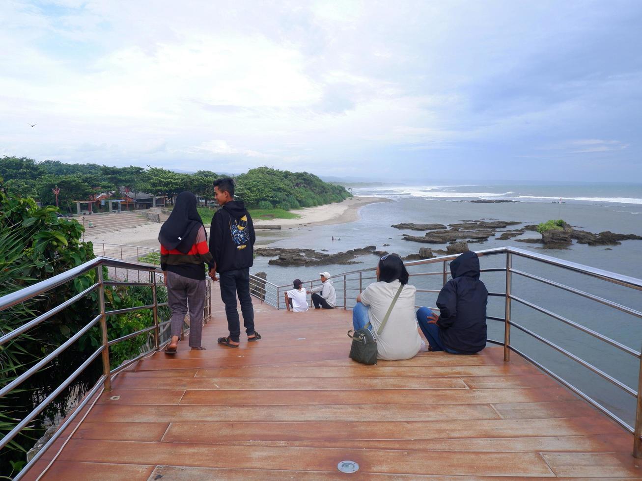 garut, indonesia, diciembre 12,2022 personas sentadas o recreativas en la carretera o puente o escaleras de madera en la playa, vista del puente de la playa en sayang heulang indonesia foto