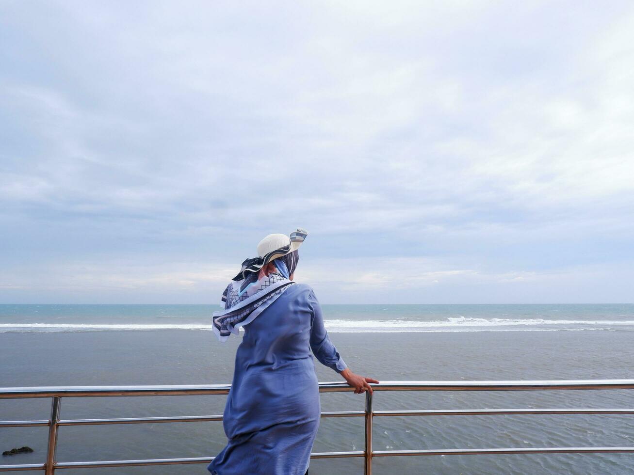 Back of the woman in the hat on the tropical beach who was looking at the sky and the sea from the bridge. sea view photo