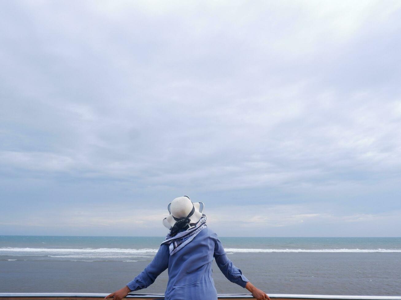 Back of the woman in the hat on the tropical beach who was looking at the sky and the sea from the bridge. sea view photo