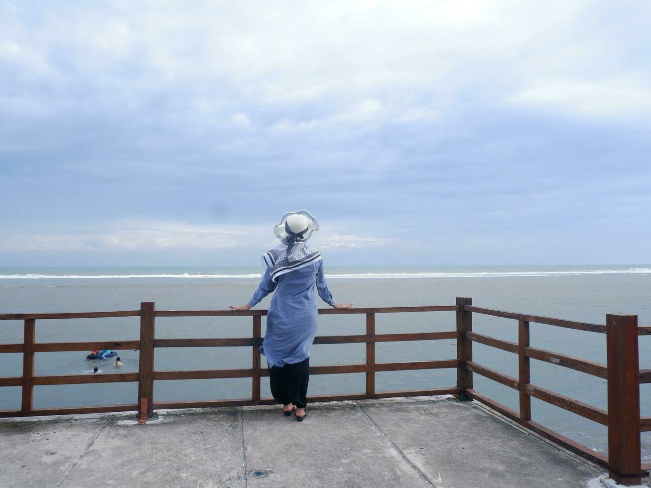 Back of the woman in the hat on the tropical beach who was looking at the sky and the sea from the bridge. sea view photo