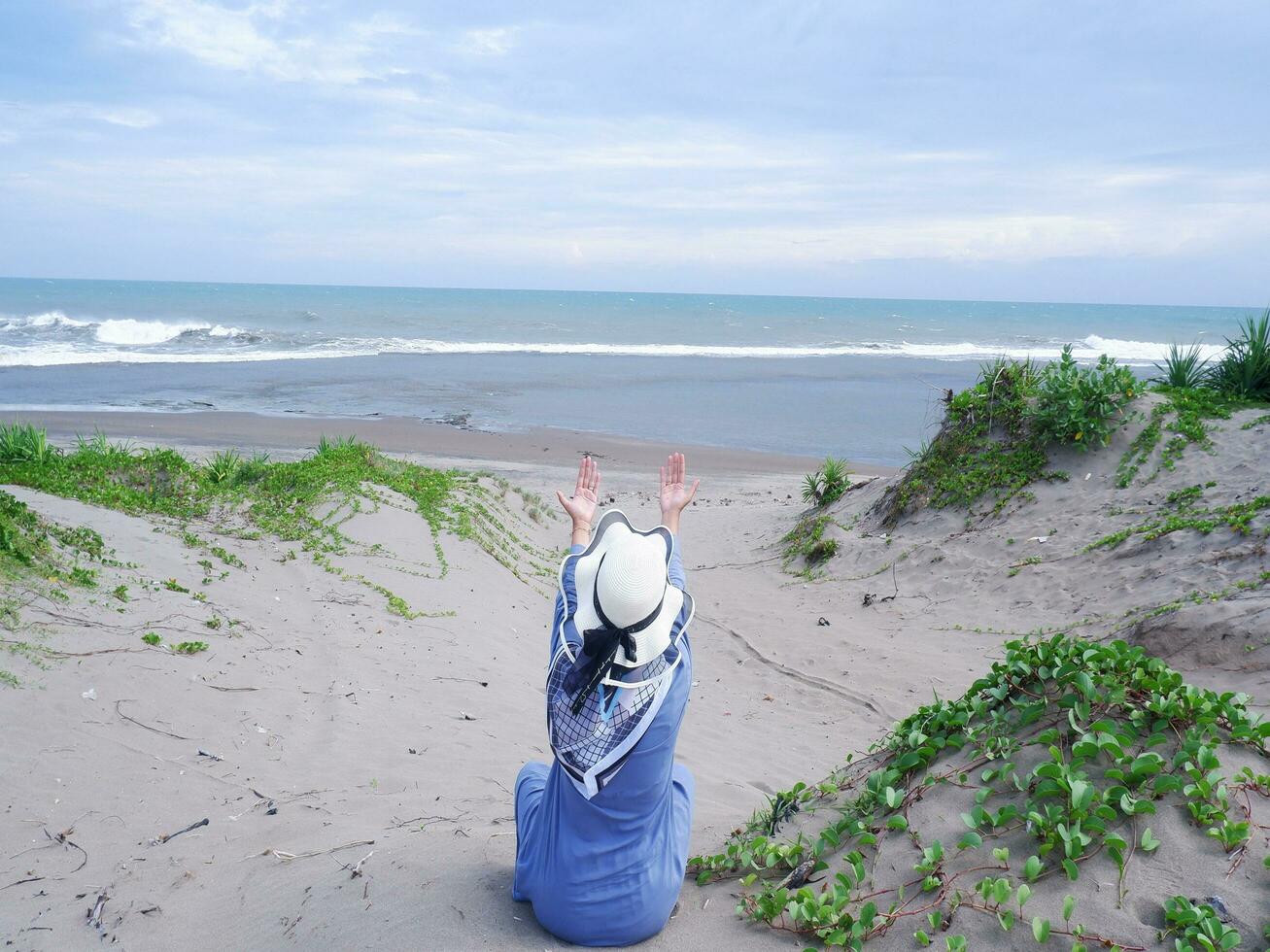 Back of woman in the hat on the tropical beach who was sitting on the sand and looking at the sky and the sea, while spreading her arms . happy women.Beach view photo