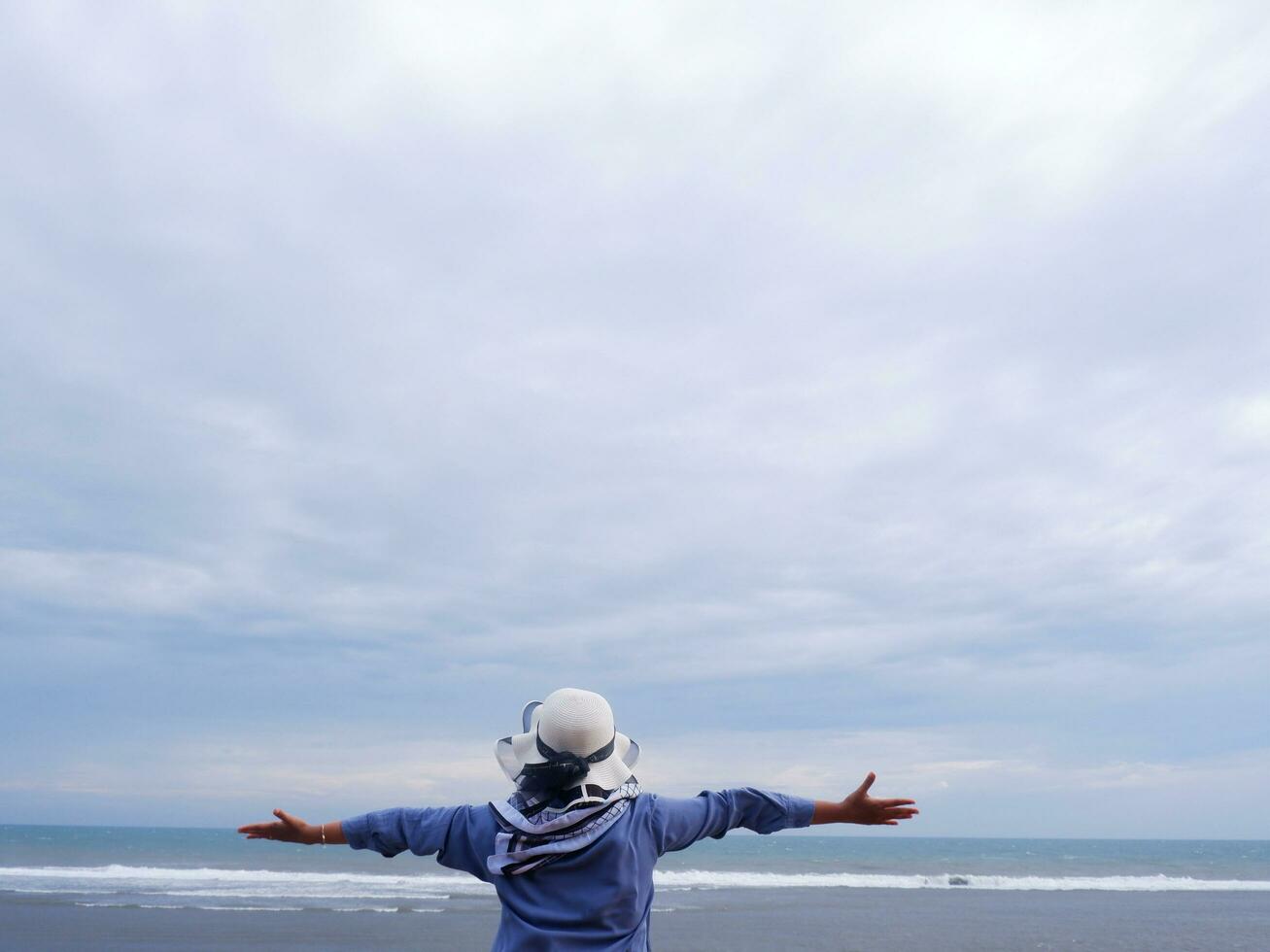 Back of the woman in the hat on the tropical beach who is looking up at the sky and the sea photo