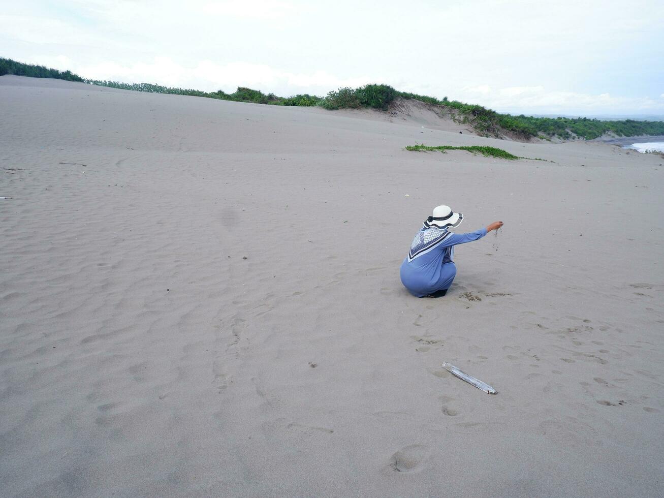 espalda de la mujer en el sombrero que estaba sentada y jugando arena de playa, la vista de la arena foto