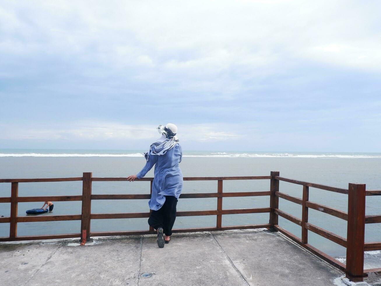 Back of the woman in the hat on the tropical beach who was looking at the sky and the sea from the bridge. sea view photo