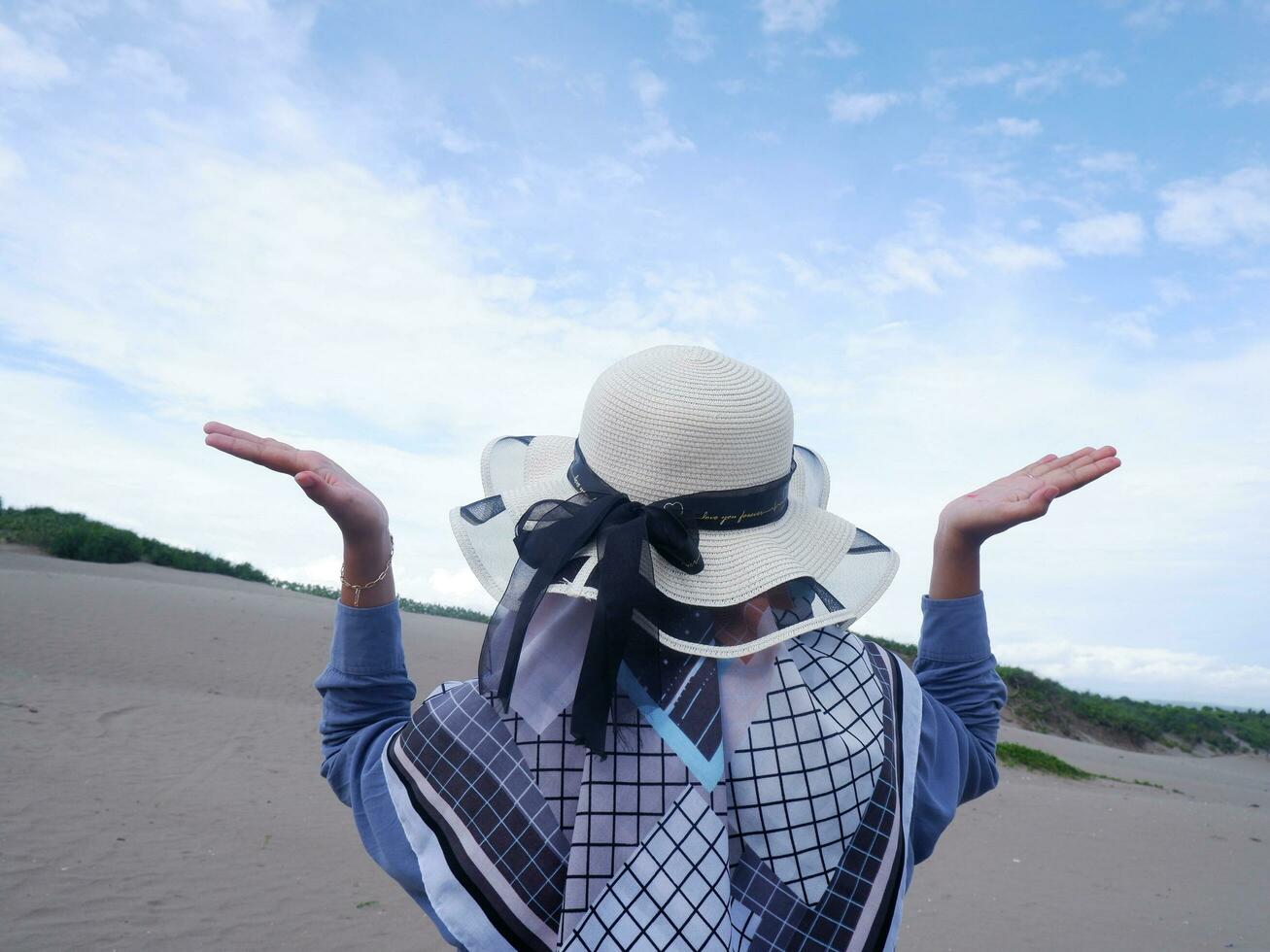 Back of the woman in the hat on the tropical beach who is looking up at the sky and the sea photo