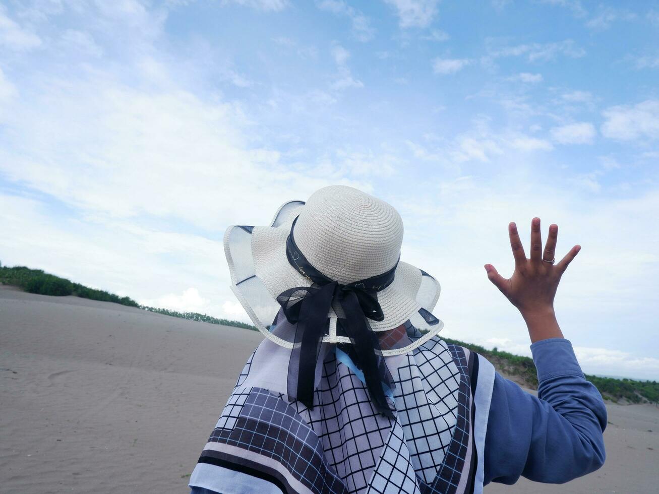 Back of the woman in the hat on the tropical beach who is looking up at the sky and the sea photo
