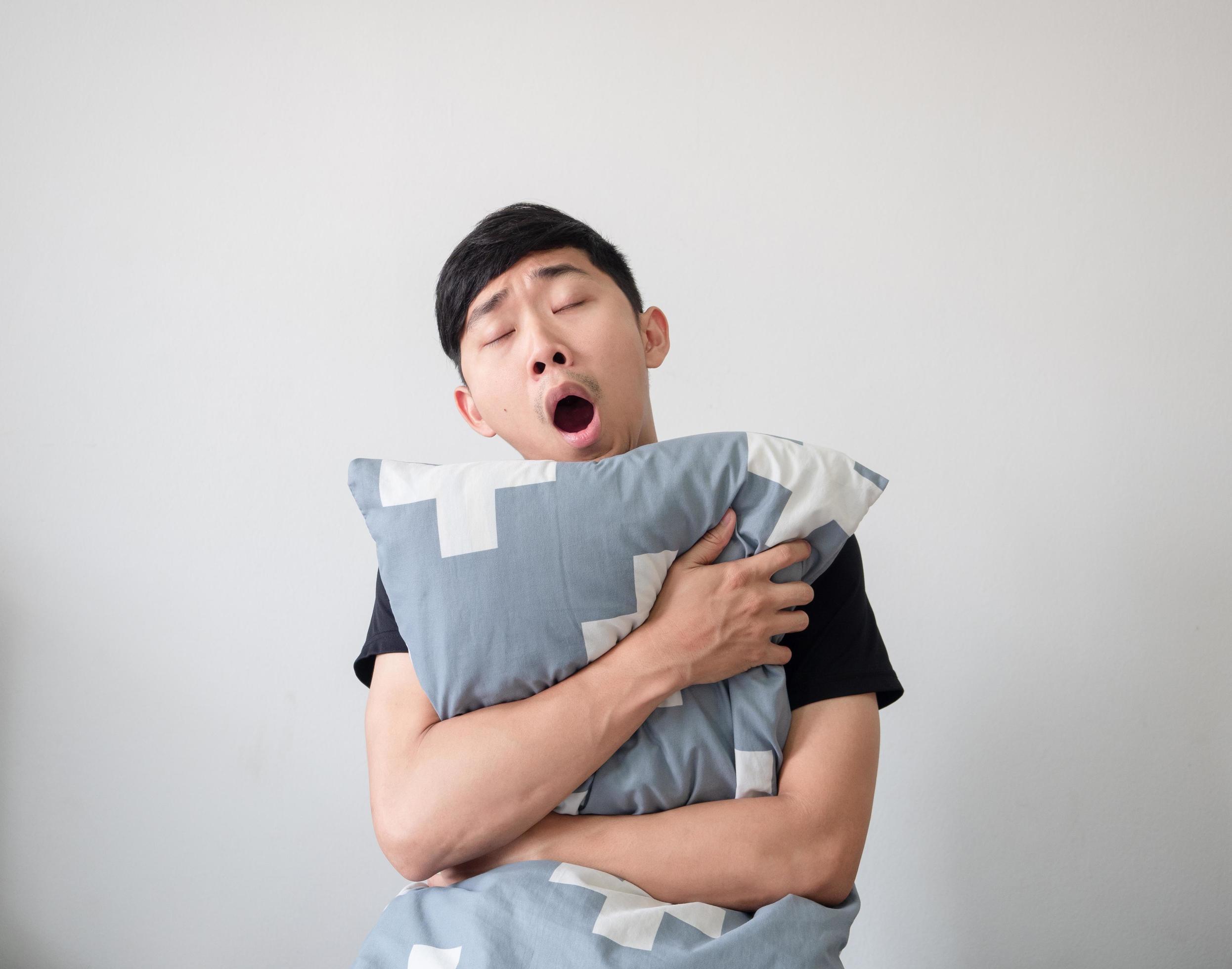 Asian young man wake up and hugging pillow yawn and feel sleepy on