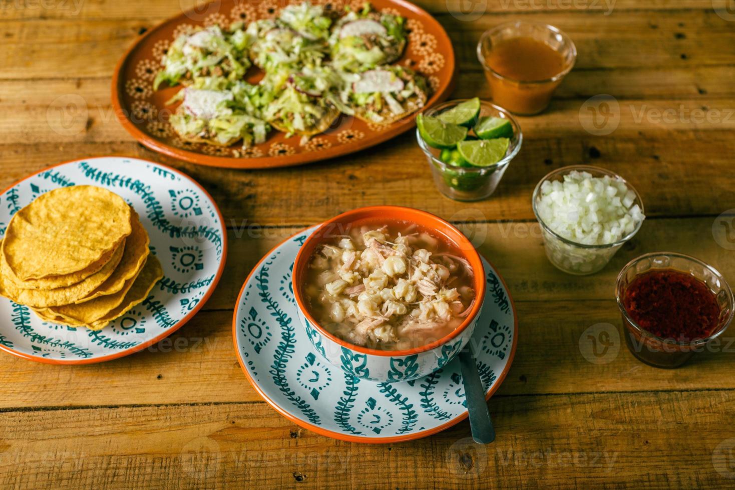 pozole servido en plato hondo, con tostadas, salsa y vegetales en una mesa de madera. comida típica mexicana. foto