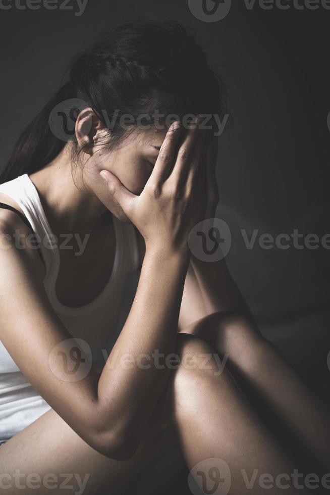 A woman hiding face. Violence against women concept. Depressed teenager sitting holding head in hands, stressed sad young woman having mental problems. photo