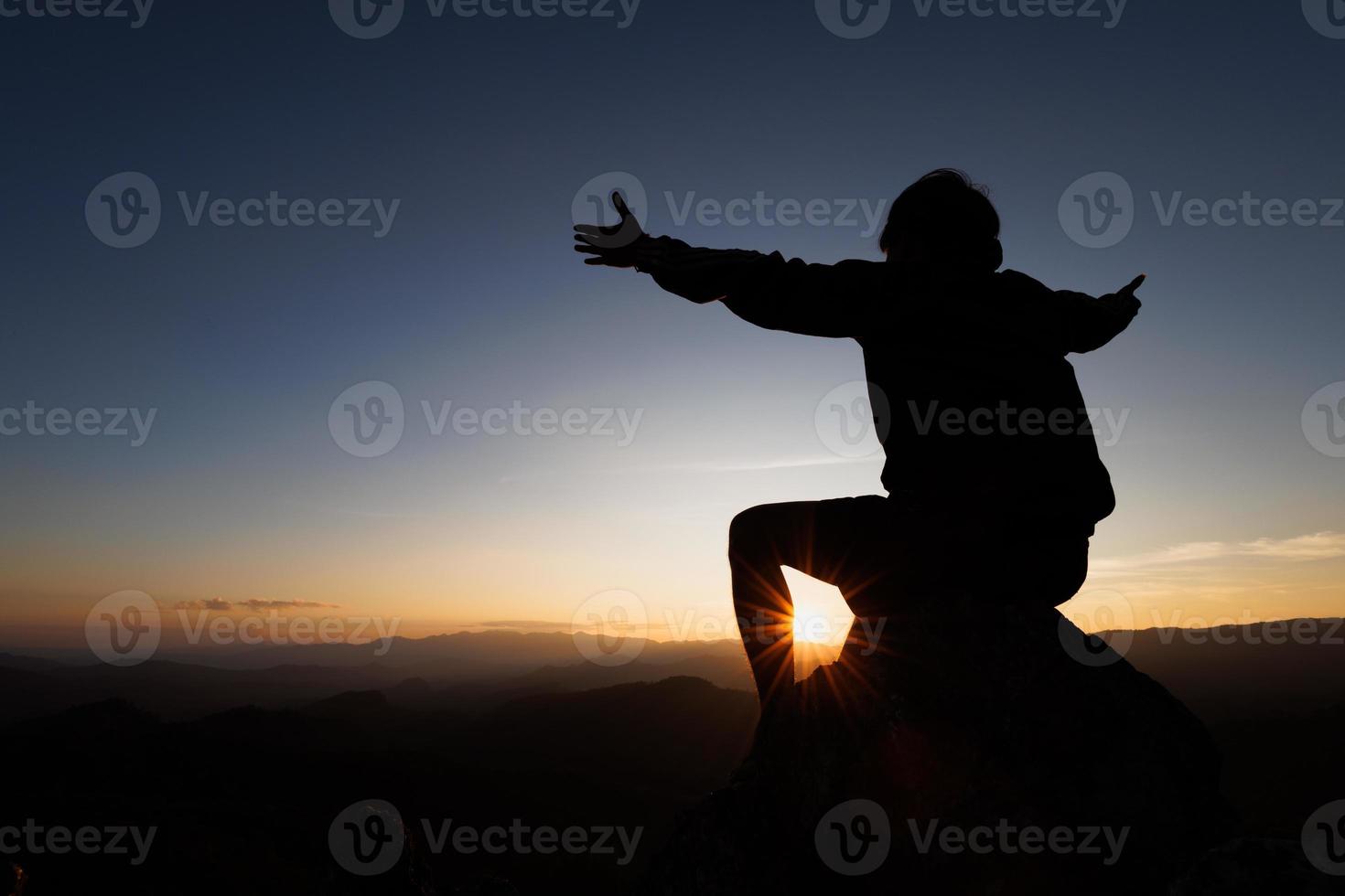Silhuette Young Woman praying on the mountain, arms outstretched observing a beautiful dramatic sunrise. photo