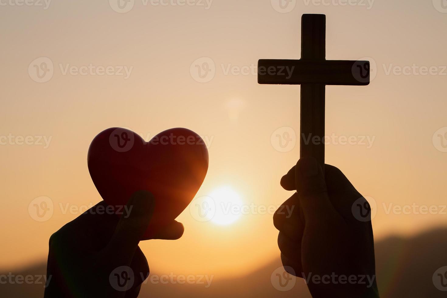 Silhouette of woman hands praying with cross and holding a red heart ball  in nature sunrise background,  Crucifix, Symbol of Faith. Christian life crisis prayer to god, The concept of loving God. photo