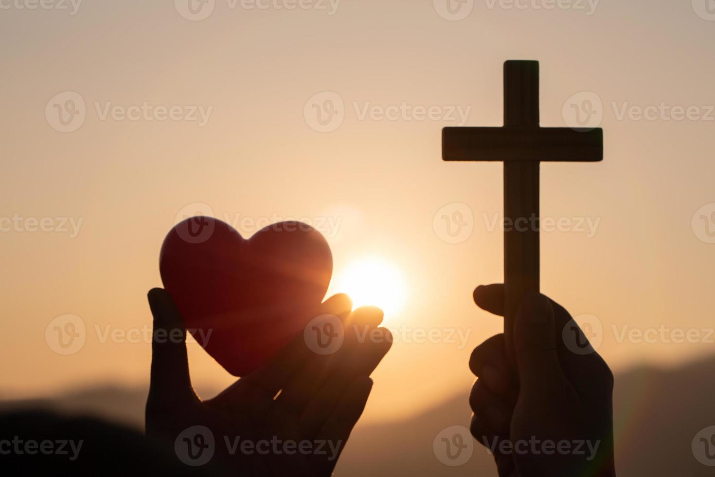 Silhouette of woman hands praying with cross and holding a red heart ball  in nature sunrise background,  Crucifix, Symbol of Faith. Christian life crisis prayer to god, The concept of loving God. photo