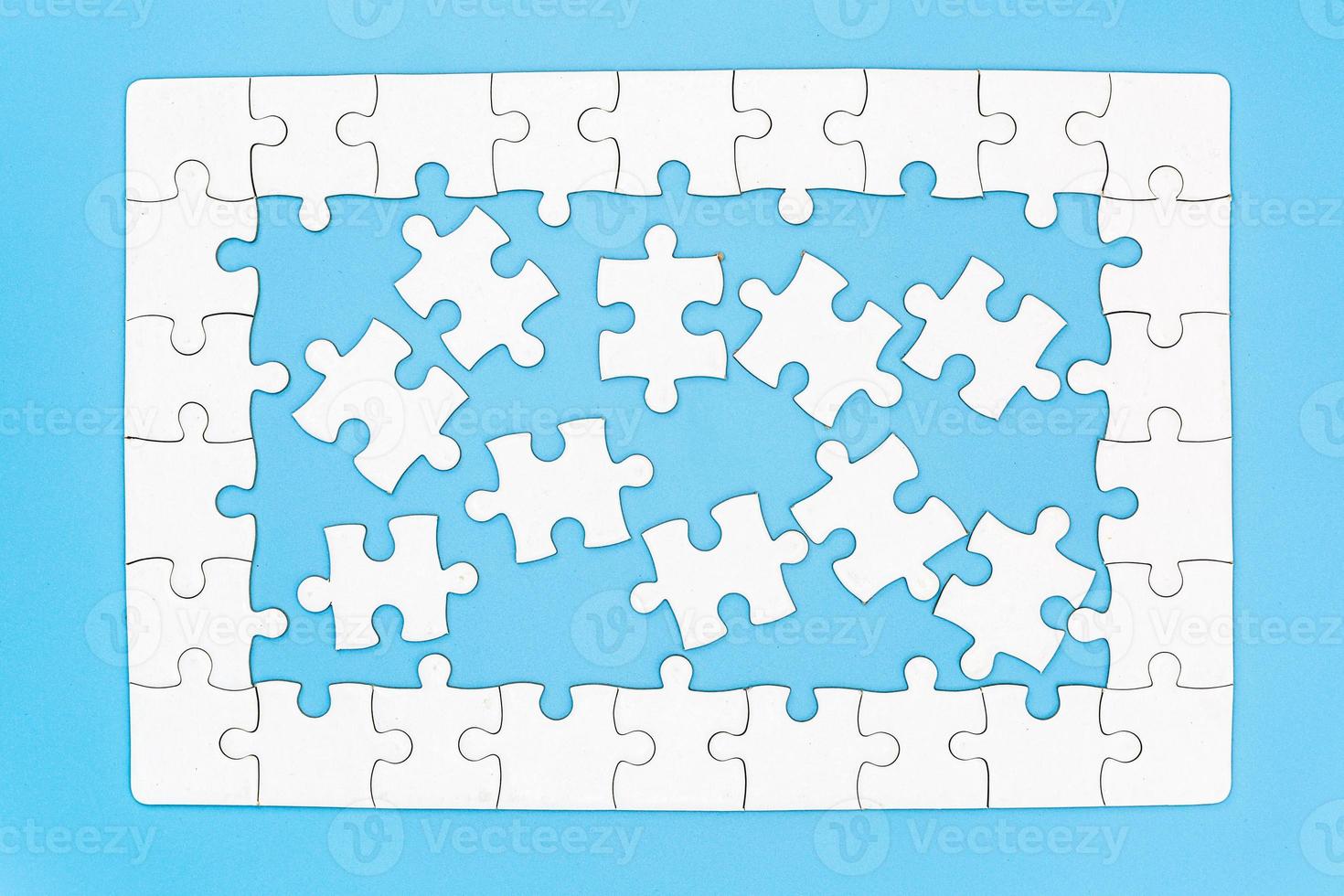 Unfinished white jigsaw puzzle on blue background with copy space. Business strategy teamwork and problem solving concept. photo